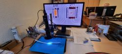 Digital microscope with a display showing electronic components on a desk in an office.