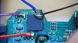 Close-up of a circuit board with soldered wires and a needle positioned on a pin.