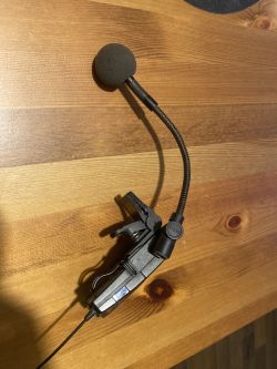 Mikrofon z elastyczną gęsią szyjką i klipsem umieszczony na drewnianym stole.