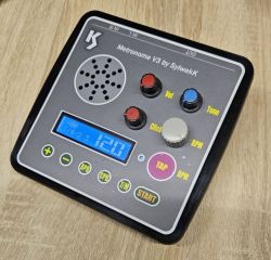 Elektroniczny metronom w czarnej obudowie z ekranem LCD, czterema pokrętłami i kolorowymi przyciskami.