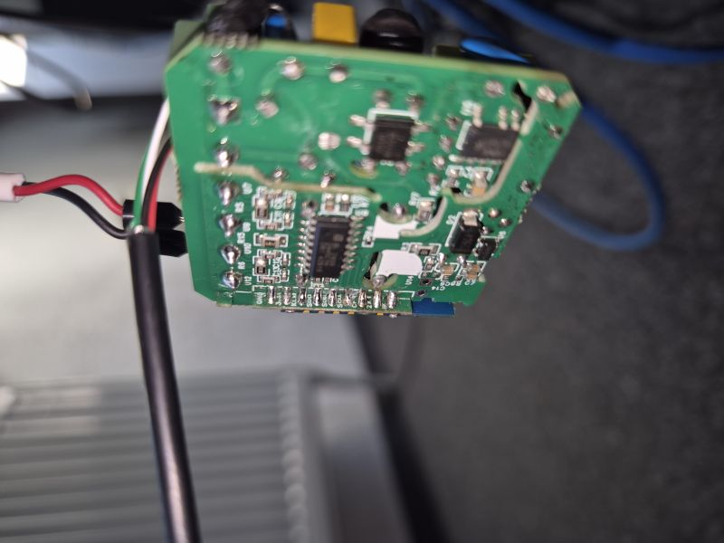 Close-up of a green PCB with SMD components and attached wires; blurred background.