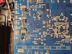 Zbliżenie na niebieską płytkę drukowaną z widocznymi komponentami elektronicznymi i oznaczeniami.