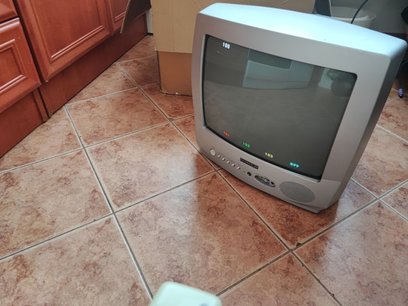Telewizor kineskopowy Daewoo K14C5GT na tle podłogi z kafelkami, widać ekran z wyświetlonymi kanałami.