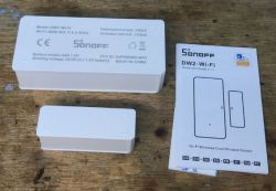 Sonoff DW2-Wi-Fi Door Sensor with Manual Sonoff DW2-Wi-Fi door sensor on a wooden surface with a user manual.