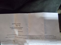 Pognieciona kartka z wydrukowanym pismem po polsku, sfotografowana do góry nogami na ciemnym tle