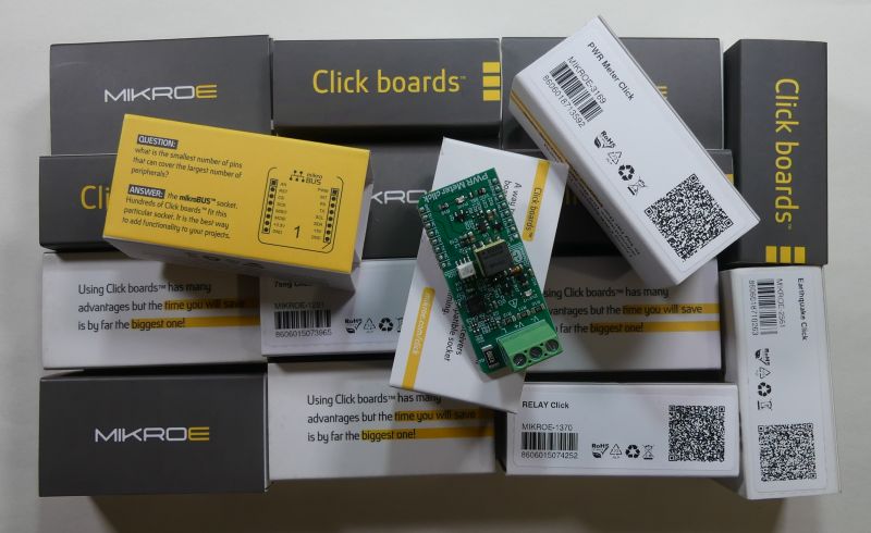 Zestaw modułów Click Boards z płytką rozszerzeniową MIKROE na tle pudełek.