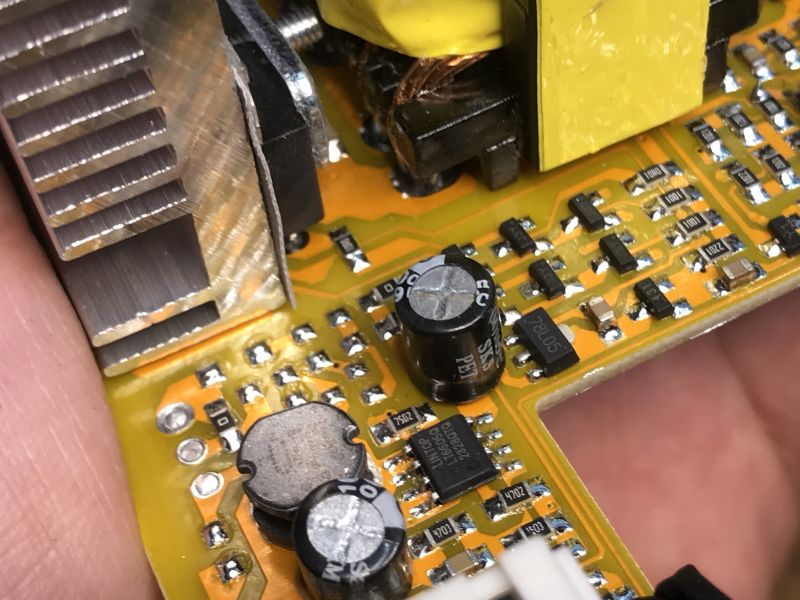 Zbliżenie na wnętrze przetwornicy samochodowej, ukazujące różne elementy elektroniczne na płytce PCB, w tym kondensatory i układy scalone.
