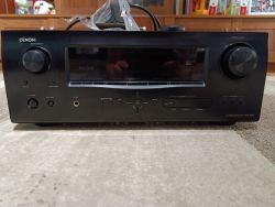 Amplituner Denon AVR-1910 ustawiony na dywanie, widoczny z przodu.