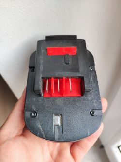 Zbliżenie na spód czarno-czerwonej baterii Black&ampecker 12V z widocznymi metalowymi stykami.