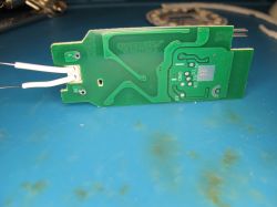 PCB with connected wires lying on a blue workspace Green circuit board with visible traces and two connected white wires on a blue surface