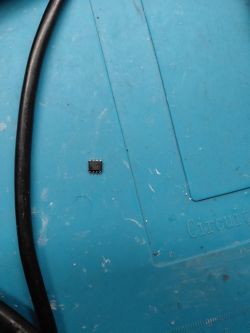 Small 8-pin IC chip lying on a blue anti-static work mat.