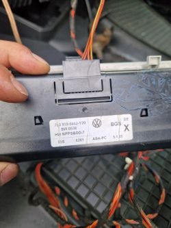 Osoba trzyma moduł elektroniczny z naklejką Volkswagena i odsłonięty wiązek przewodów.