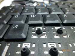Zbliżenie na klawiaturę laptopa z częściowo zdemontowanymi klawiszami, widoczne gumowe kopułki i zabrudzenia.