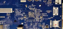 Zbliżenie na niebieską płytkę drukowaną z wieloma oznaczeniami i komponentami elektronicznymi.