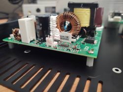 Płytka elektroniki z cewką toroidalną i kondensatorem; czerwone kółko wskazuje mały element SMD