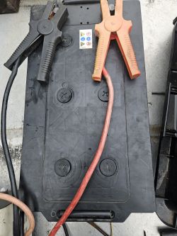 Akumulator z kablami rozruchowymi i trzema zauważalnymi korkami.