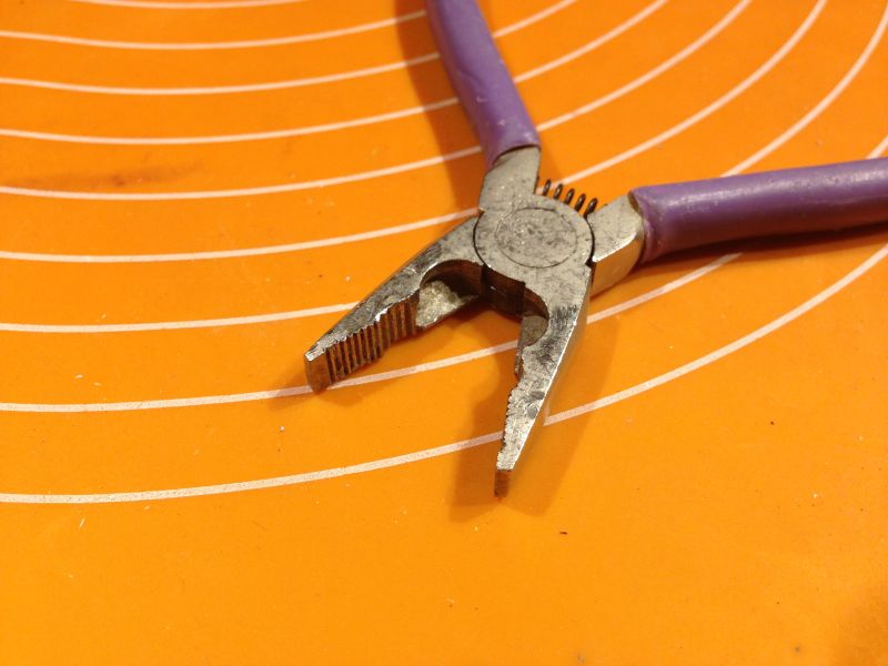 Zużyte kombinerki z fioletowymi uchwytami na pomarańczowej powierzchni