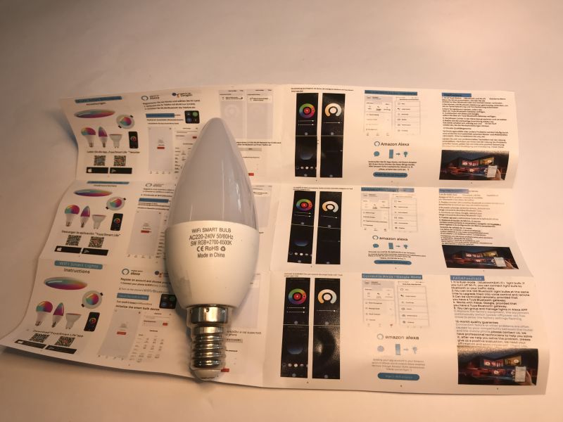 WiFi Smart Bulb and Opened User Manual Candle-style WiFi smart bulb lying on an opened user manual with color diagrams.