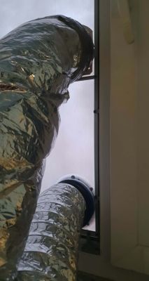 Two flexible silver AC hoses connected to a window insert with round duct fittings.