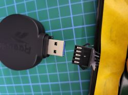 Bluetooth dongle Reebok i 5-pinowe złącze PCB na tle zielonej maty.
