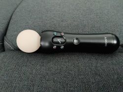 Kontroler Sony PlayStation Move leży na szarej, materiałowej kanapie.