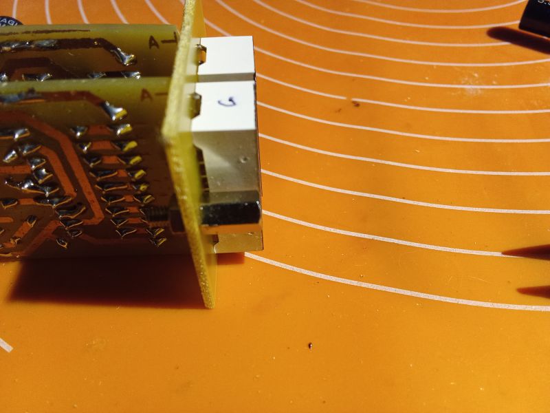 Close-up of a printed circuit board with conductive tracks and soldered components, placed on an orange surface with white circles.