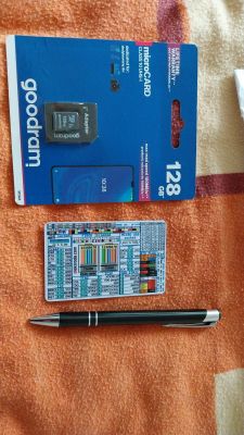 Goodram 128 GB microSD card with adapter, connection diagram card, and black pen on orange background.