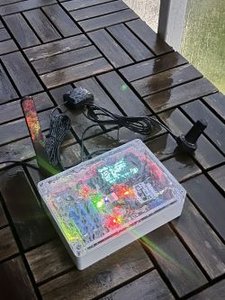 Electronic GPS Tracker on a Wooden Table Transparent electronic device enclosure on a wooden table with visible wires and an antenna.
