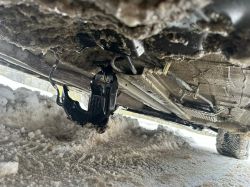 View from under a car with a black component hanging on wires.