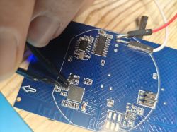 A hand holding tweezers over a circuit board with attached wires.