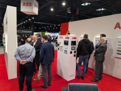 ABB trade show booth with several people talking near white display panels with screens on a red carpet.