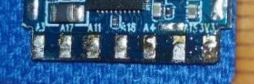Close-up of bottom edge of blue PCB with eight pins and alphanumeric labels.