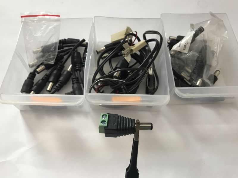Three containers with various DC Jack connectors and a screw terminal adapter held by pliers in the foreground.