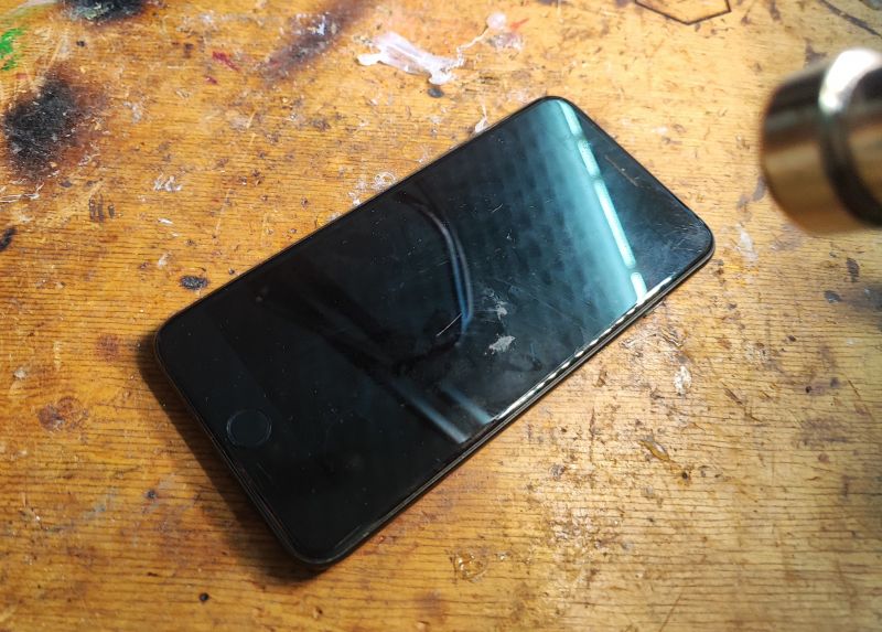Preparing for iPhone Battery Replacement iPhone lying on a wooden workbench next to hot air for screen heating