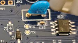 Zbliżenie płytki PCB z niebieskim elementem „102 2kV”, padami RX/TX i układem scalonym U12