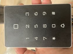 Zamek kodowy z panelem dotykowym trzymany w ręce, widoczne cyfry i symbole