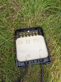 Moduł elektroniki z tyłu panelu fotowoltaicznego, z otwartą pokrywą na trawie