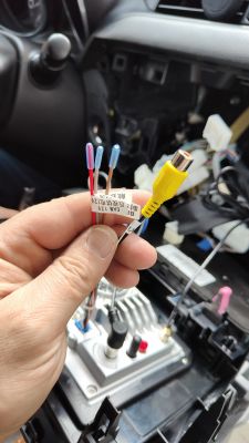 Ręka trzymająca wtyczki i przewody elektryczne nad tyłem radia samochodowego.