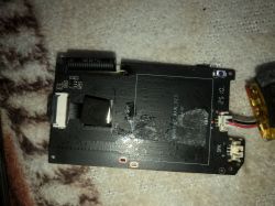 Black PCB with connectors, wires, and a small battery on patterned fabric background