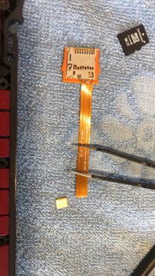 Uszkodzona taśma FFC z urwanym końcem obok slotu microSD na niebieskim materiale