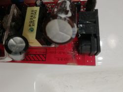 Zbliżenie na płytkę drukowaną z widocznymi elementami elektronicznymi, w tym kondensatory i transformator.