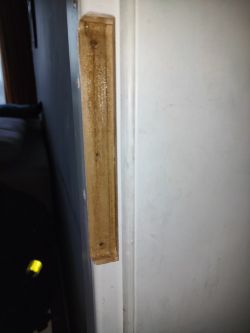 Side view of a wooden strip attached to a door with visible screw holes filled with putty.