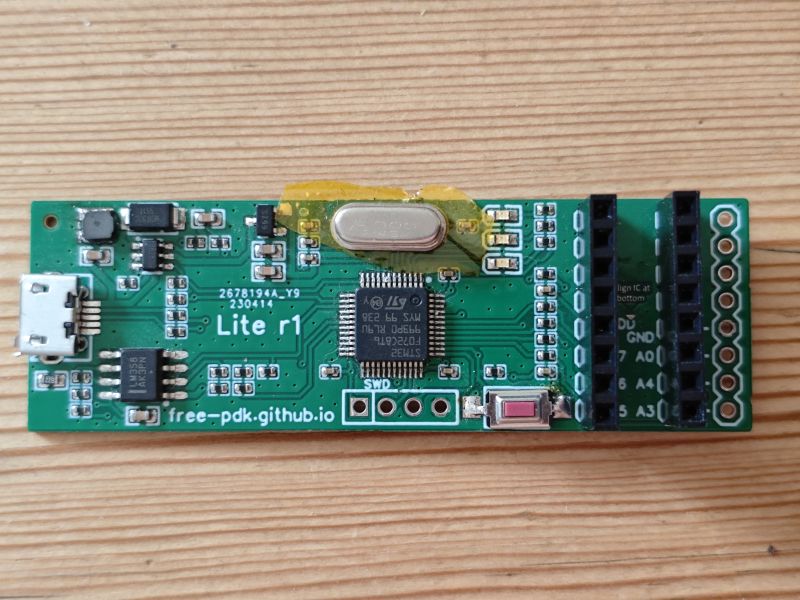 Green Lite r1 PCB with micro-USB port, IC chip, and pin headers on a wooden surface