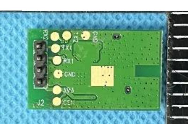 Green PCB module with header pins and solder pads labeled RX0, TX1, GND, 3V3, EN