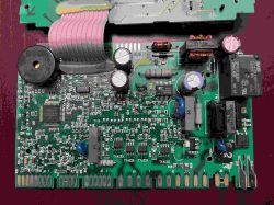Zbliżenie na płytkę drukowaną ze zmywarki z widocznymi elementami elektronicznymi, kondensatorami i złączami.