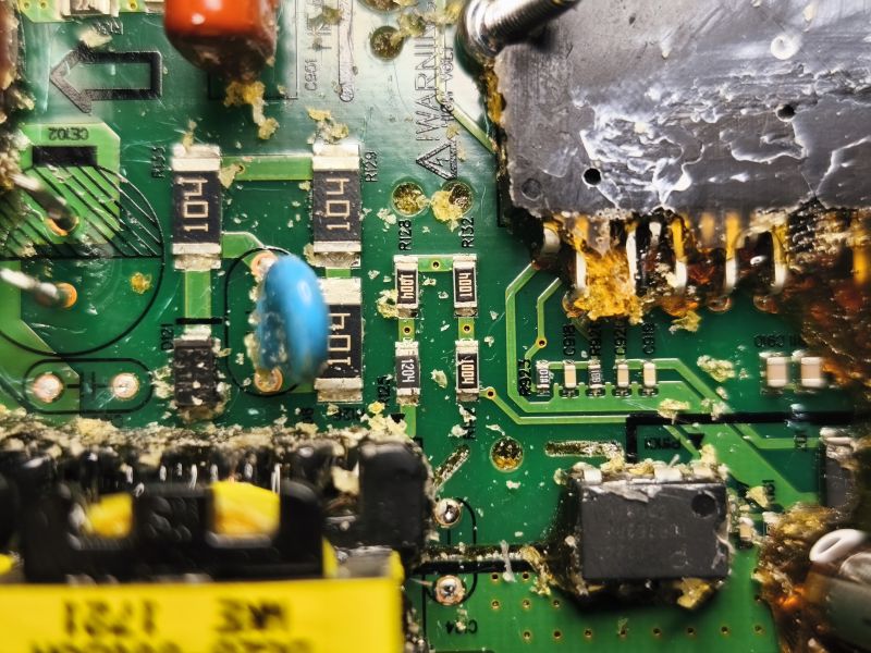 Zbliżenie na uszkodzony układ elektroniczny z widocznymi rezystorami i kondensatorami