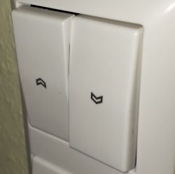 White Wall Switch with Arrow Buttons White wall switch with two buttons marked with arrows.