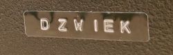 Metal tape with embossed “DZWIEK” label on a black textured background