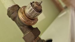 Zbliżenie na korpus starego zaworu grzejnikowego Danfoss z widocznym metalowym gwintem i trzpieniem.