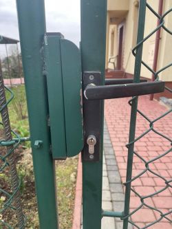 Zbliżenie na zamek w metalowej furtce z zamontowanym uchwytem.